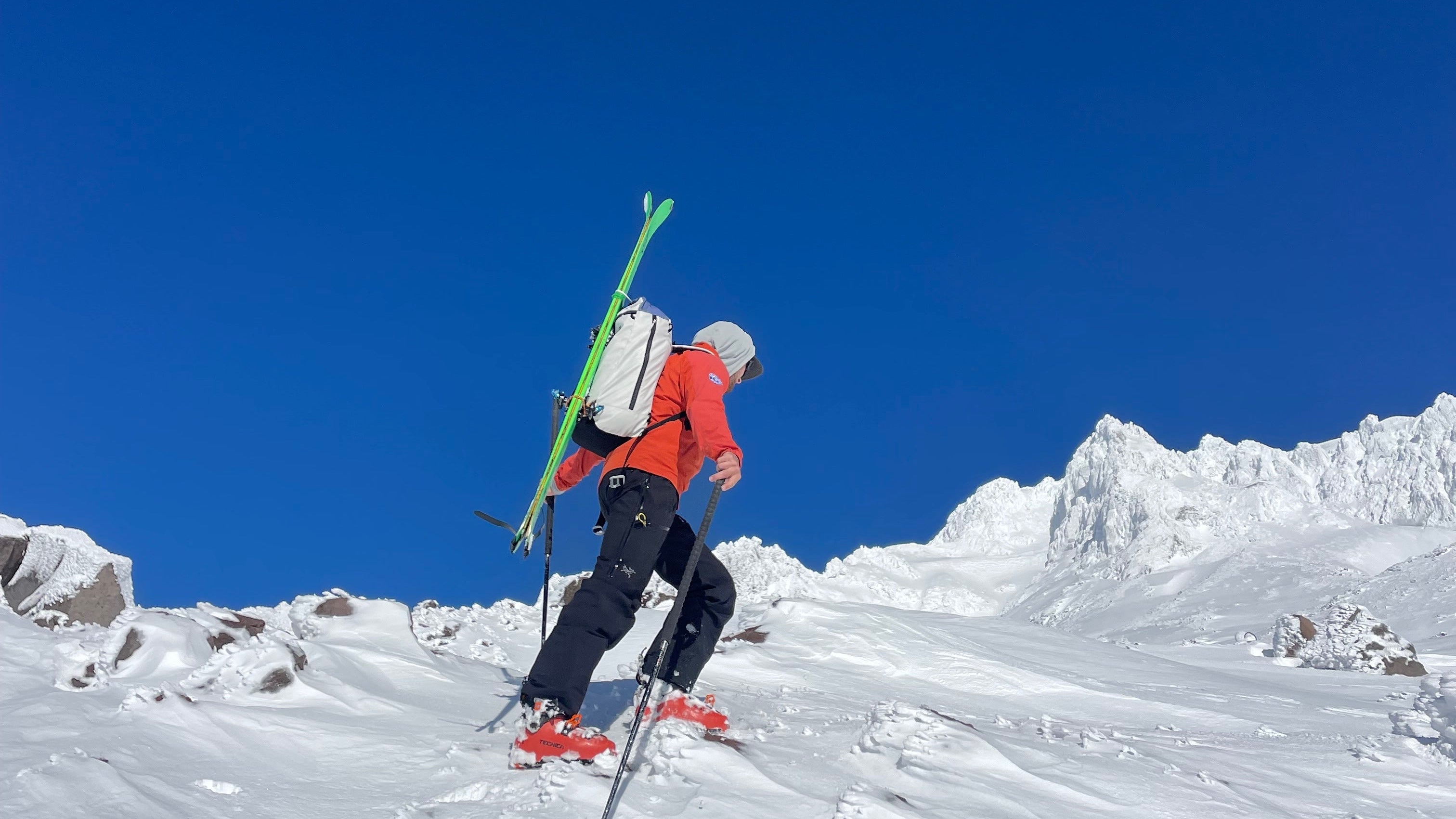 A person with skis and a backpack is climbing a snowy mountain. The backpack is coated with PolyCores Eco-Shield. 