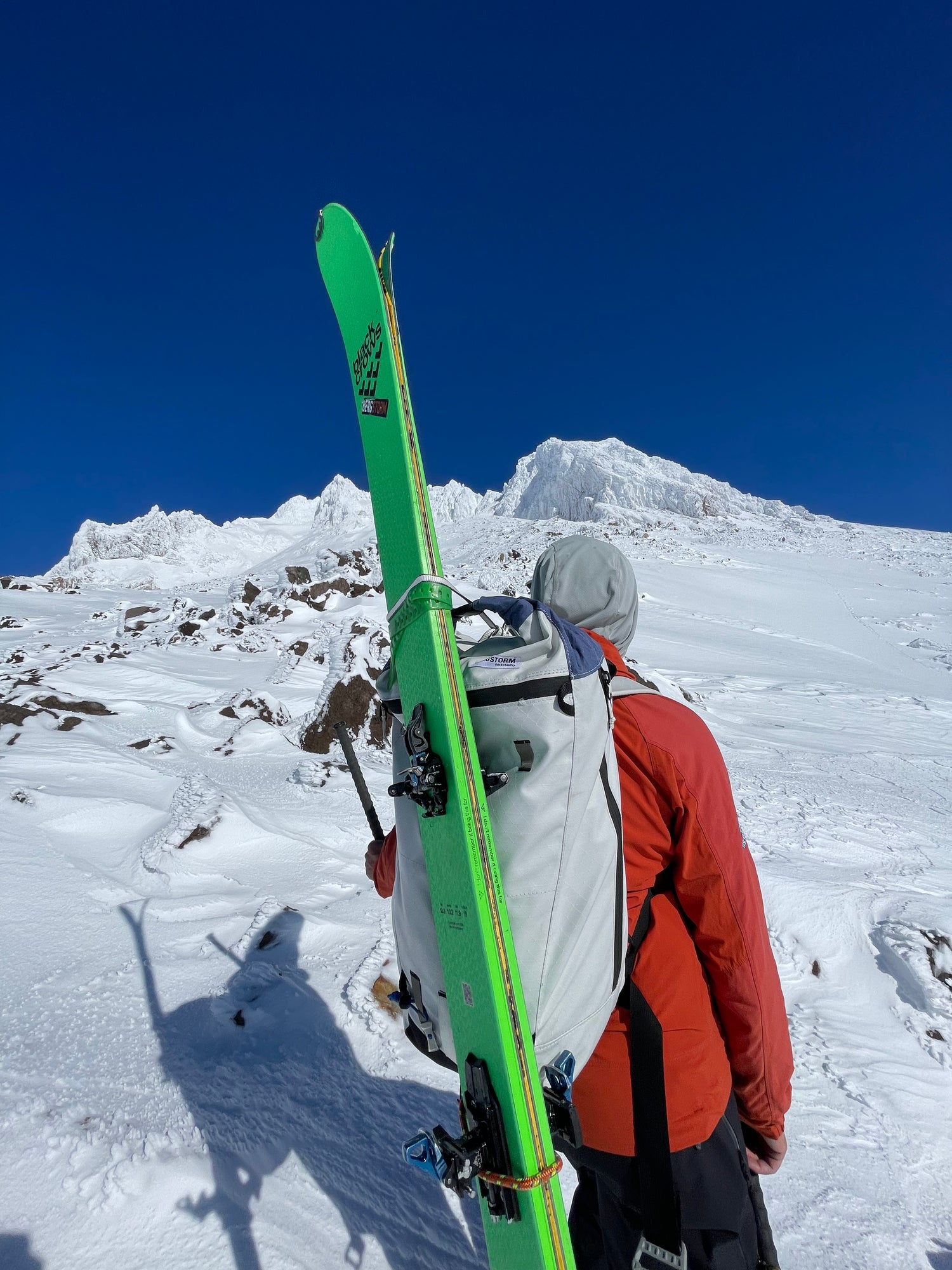 A person with skis and a backpack is climbing a snowy mountain. The backpack is coated with PolyCores Eco-Shield. 